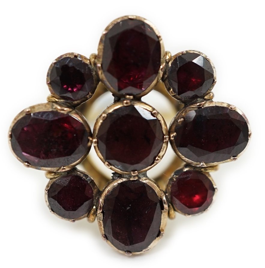 A late Victorian gold and nine stone garnet cluster set dress ring, of flower head design, set with round and oval cut stones, size L, gross weight 6.4 grams. Condition - poor to fair